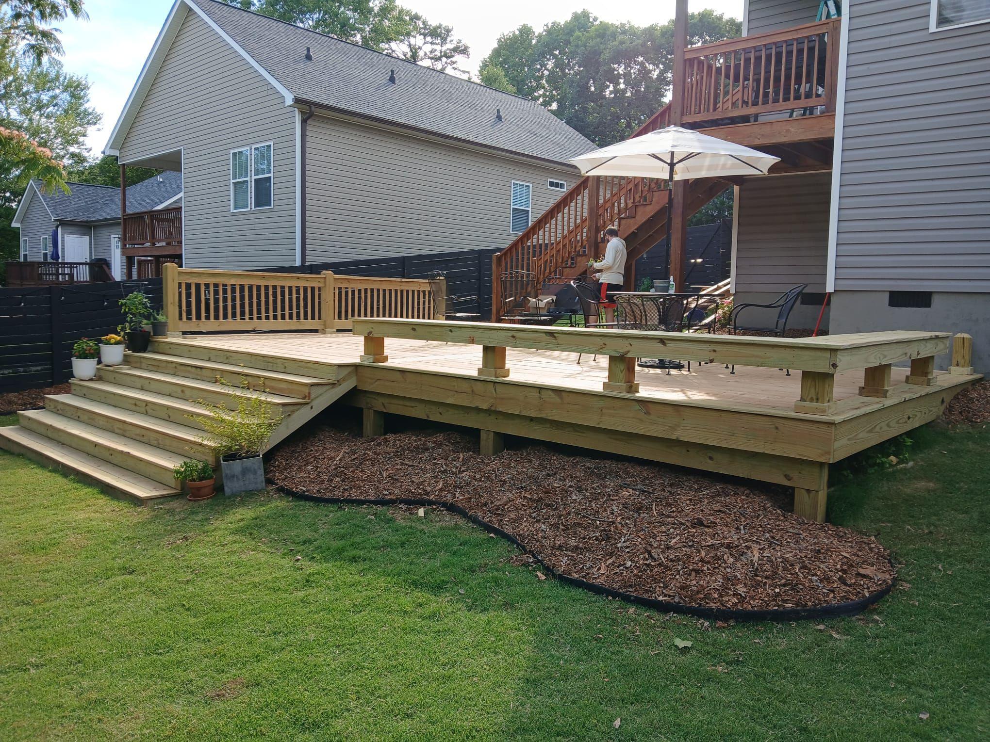Finished backyard deck with wide steps down to the lawn, a bench along the edge and a curved mulch bed