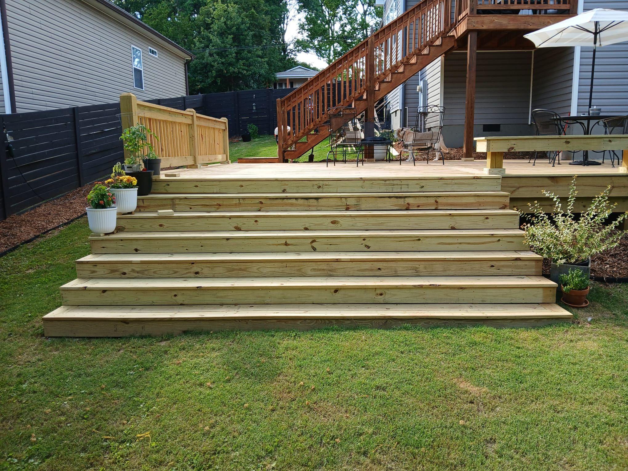 Broad multi-step stairs leading from the lawn up to a new pine deck with potted plants