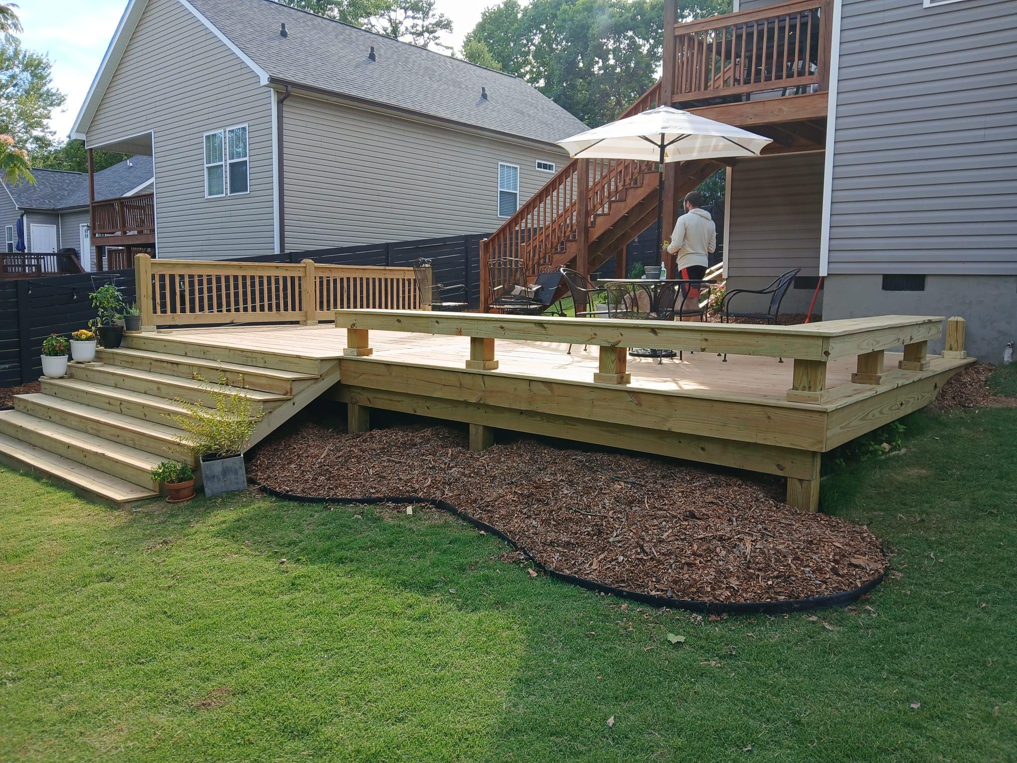 Raised pine deck with a built-in bench, railing and wide side stairs above a curved mulch bed in a Greenville backyard